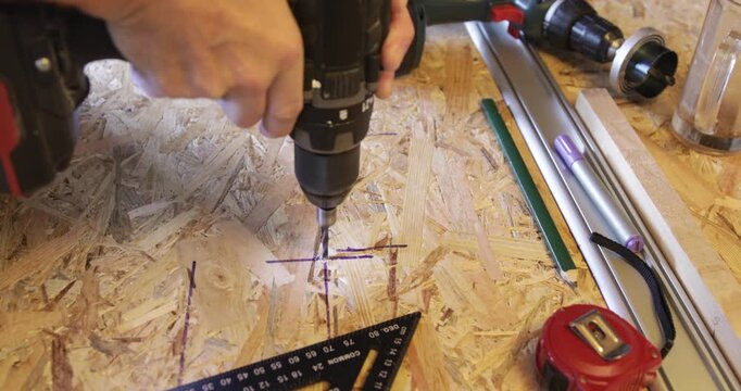 Carpenter drilling hole at OSB panel using cordless electric drill 
