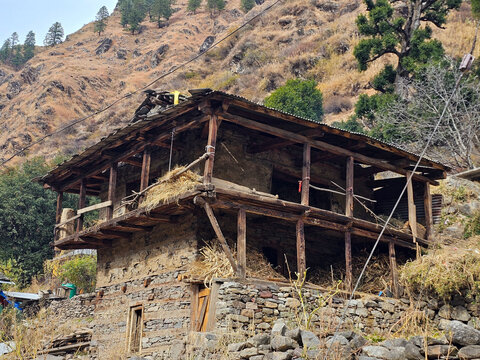 Horizontal Landscape View of Traditional Two-Story Himalayan Stone and Wood House with Open Balconies and Hay Storage on Rocky Mountain Slope in Himachal Pradesh.