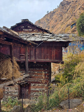 Vertical View of Traditional Two-Story Himalayan Stone and Wood Village House with Slate Tiled Roof and Hay Storage on Mountain Slope in Himachal Pradesh.