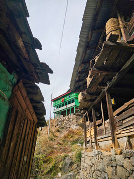 Vertical Low Angle View of a Narrow Village Alleyway Between Traditional Wooden and Stone Houses Leading to a Green Building in Parvati Valley Himachal Pradesh India.