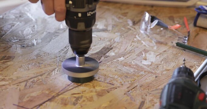 Carpenter - woodworker cuts hole through OSB plate using cordless drill and circular hole saw attachment 