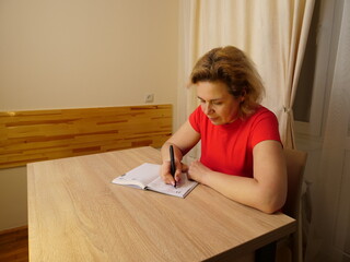 Woman writes notes in diary at table in warm home setting evening.