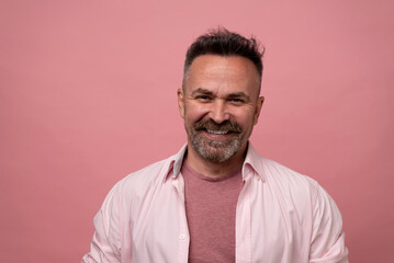 Fototapeta premium Senior handsome bristle man in pastel-pink shirt smiling cheerfully posing isolated on pink studio background. Copy space Banner Mockup. People emotions Lifestyle concept