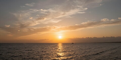 Fototapeta premium Golden sunlight pierces through clouds over rippling sea at sunset with distant ship
