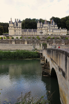 View of the Ch&acirc;teau d'Uss&eacute; rising above the river with a stone bridge in the foreground. Elegant French architectural landmark featuring historic towers, fortified walls, and landscape