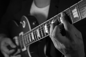 Black and white close up of electric guitar performance, guitarist fingers playing on fretboard.
