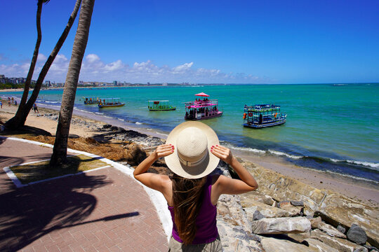 Holidays in Maceio, Brazil. Back view of woman looking jangadas rafts going to natural swimming pools of Ponta Verde, Maceio, Brazil.