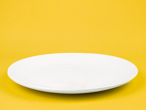 An empty white plate isolated on yellow background