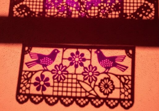 Cut paper garland shadow on an orange wall. Traditional Mexican art for festive decoration. Folkloric design with bird and flower patterns.