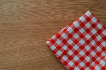 Obraz premium Red Gingham Napkin on Wood: A red and white gingham napkin sits on a wooden surface, exuding simplicity and elegance, evoking feelings of comfort, and the simplicity of everyday life.