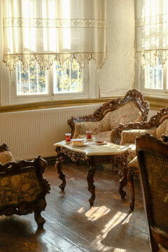 Cozy afternoon tea setup in a historic living room interior, featuring antique carved wood furniture, elegant marble table, and sunlight streaming through sheer curtains.