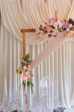  Elegant wedding photo zone decoration with pastel flowers, wooden arch, draped beige curtains, and crystal candelabra with artificial candles.