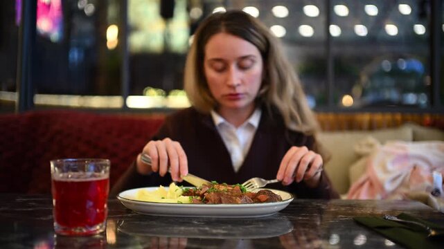 Woman eating mashed potatoes and meat at a restaurant table using fork and knife