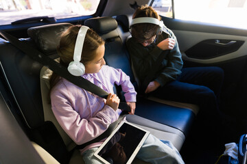 Teens wearing headphones and using tablet in car, fastening seat belt during family road trip