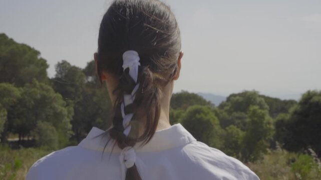 Back view close up of a young woman in a white linen dress strolling through a rustic landscape with a straw basket for a sustainable picnic al fresco 