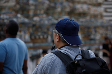 Obraz premium Man tourist wearing a cap and a backpack walking and sightseeing, rear view behind, at Wat Arun.