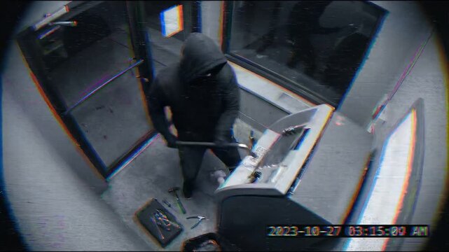 Surveillance footage showing a hooded figure attempting to break into an ATM in a dimly lit area, conveying a sense of tension and crime