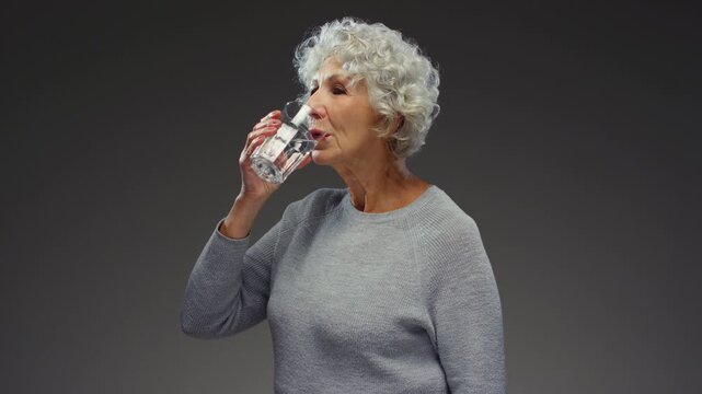 Elderly woman holding glass of water on hand, for wellness. Senior female drinks water, hydration. Old person, drinking beverage. Retirement with liquid, fluid and minerals, hydration and detox