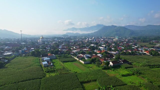Beautiful aerial drone footage of the neighbourhoods  of Mataram city, in Lombok island, Indonesia, at sunrise, with 2 big beautiful mosque, many houses, trees and mountains, with green rice fields