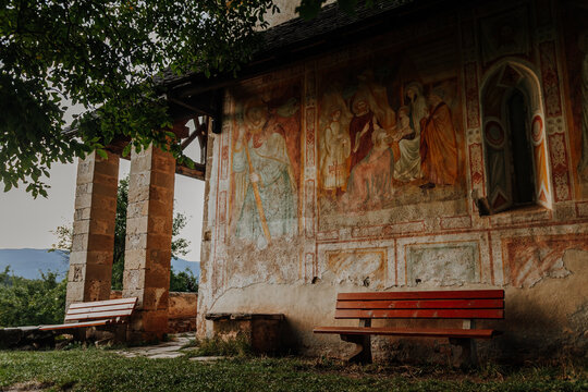 Ancient religious frescoes on the exterior wall of St. Valentin church with wooden benches, South Tyrol, Italy