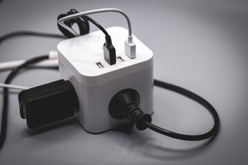 This modern, white, cube-shaped charger features multiple USB ports and outlets, all covered in tangled black and white cables. It&rsquo;s a sleek yet chaotic hub to keep all your devices powered.