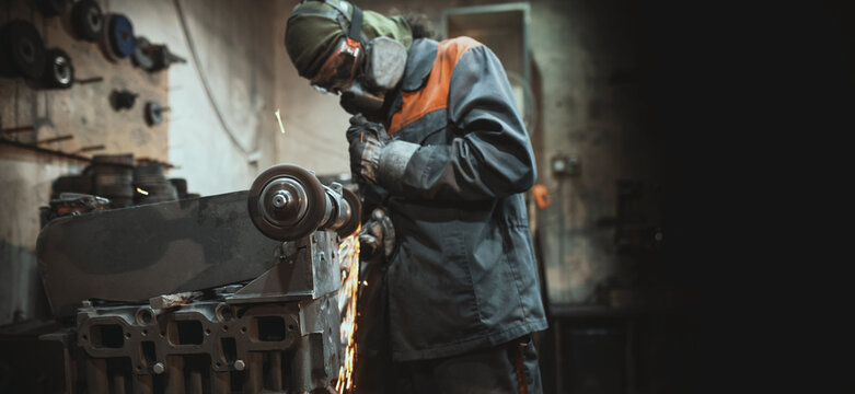 A man in protective gear, mask, and gloves grinds metal by hand in a workshop  stationary grinding machine (bench grinder). selected focus banner copy space