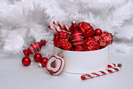 A set of red glass Christmas tree ornaments in a round box against a white Christmas tree. Single-color New Year's decor.
