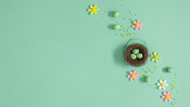 Easter nest with speckled green eggs on mint background with pastel flowers, top view, spring holiday celebration composition Easter with copy space for text, flat lay concept for greeting card design