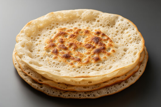 Stacked golden Lahoh pancakes with delicate holes on dark gray surface, representing Yemeni culinary tradition and communal sharing