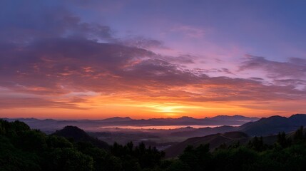 Fototapeta premium Vibrant sunrise paints the sky with color over misty mountains and lush green hills