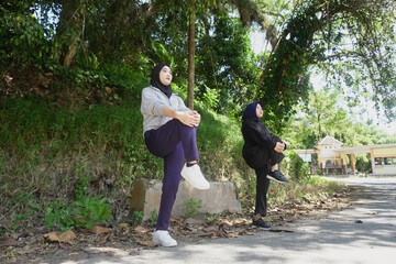 Fototapeta premium Two young Muslim women stretching and warming up during outdoor exercise on a sunny day in a green park. 