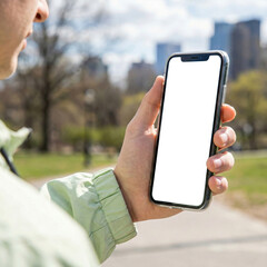 A person holds a smartphone with a blank screen outdoors in a city park, symbolizing mobile technology, communication, and modern lifestyle