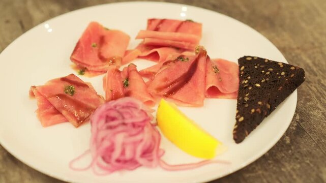 Tuna stroganina with pickled onion, lemon wedge, and rye bread on a white plate. Fresh seafood for gourmet dining, top view.