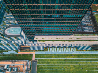 Aerial view of modern skyscraper with landscaped green park and geometric urban design, Drone top view of glass office tower with terrace lawn plaza and sustainable city space
