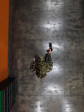 Direct overhead top-down view of a tactical shooter holding a pistol in an indoor range with night vision device.