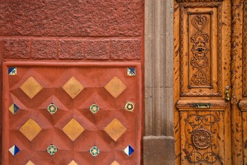 Fototapeta premium Facade view of a Colonial architecture house with a Venetian red stucco wall, a hand carved wooden door and a terracotta ceramic tile decoration, in San Miguel de Allende, Guanajuato Mexico.