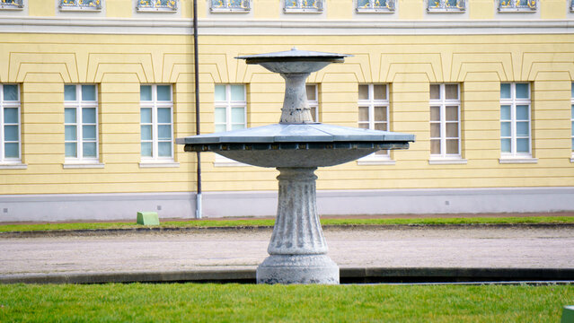 Elegant stone fountain with cascading water flows stands as a park centerpiece. Sculpted details and gentle splashes create a soothing sound amid surrounding greenery. Soft daylight reflects on rippli