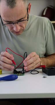 Man works in small electronics repair business and sets multimeter for service diagnostics. Tools, circuit and workflow steps. Tech services, repair process and local business promotion. Vertica