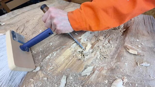 A carpenter in overalls chiselling a wooden slab in a carpentry workshop. A working man. Tools, chisel, mallet. Woodworking. Sawdust, wood chips. Real people. Lifestyle, Authentic, Candid

