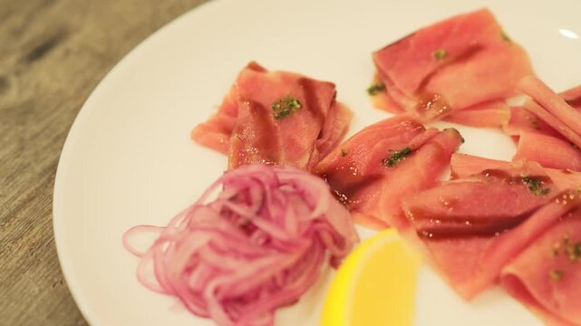 Tuna stroganina with lemon and onion slices on a white plate. Fresh raw fish dish for gourmet appetizer.