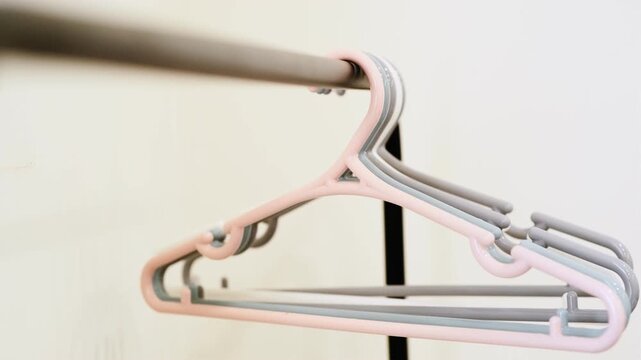 A close-up shot of a row of colorful plastic coat hangers (pink, blue, white, and purple) hanging on a black metal rack. Clean, minimalist background, perfect for lifestyle or retail imagery.
