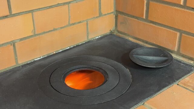 A cooktop of a newly built heating stove. The burner rings are removed, the flame in the firebox is visible. Close-up.