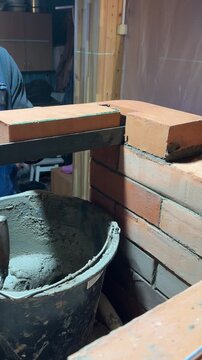 A stove master at work. Lays brick on a lintel made of angle irons. Creates a niche for the cooktop of a heating stove. Construction of a heating stove. Vertical video.