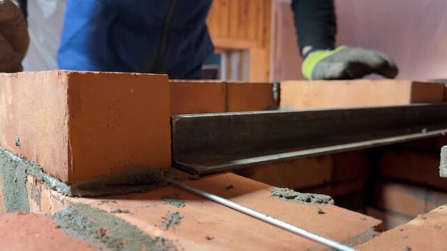 A stove master at work. Lays brick on a lintel made of angle irons. Creates a niche for the cooktop of a heating stove. Reinforced brick masonry is visible. Construction of a heating stove.