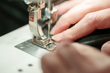 Hands work on fabric with a sewing machine in a craft space during daylight hours