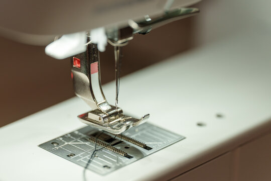 Close view of sewing machine needle and presser foot during stitching process in a workshop setting focusing on fabric work