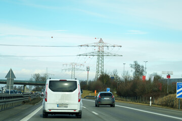 Cars drive on a highway near power lines and road signs in clear weather in a rural area during the day