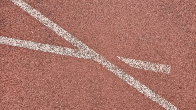 Red synthetic rubber track texture with white marking lines. Detailed texture of a resilient red athletic track with slightly worn white lane markings. Represents sports training and endurance.