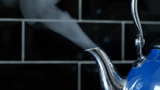 A blue kettle steams gently against a dark tiled background. The hot water vapor drifts upwards, creating a soft visual effect.