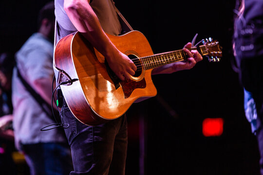 Musician playing acoustic guitar on stage during live concert